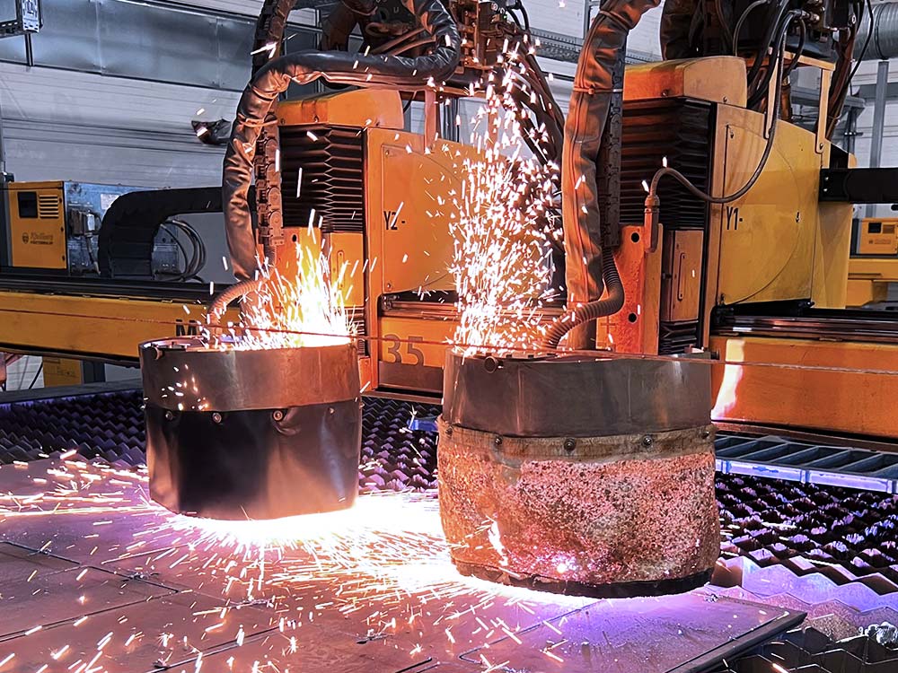 Zwei Roboteranlagen schneiden oder schweißen gleichzeitig an großen Metallzylindern, Funken fliegen.
