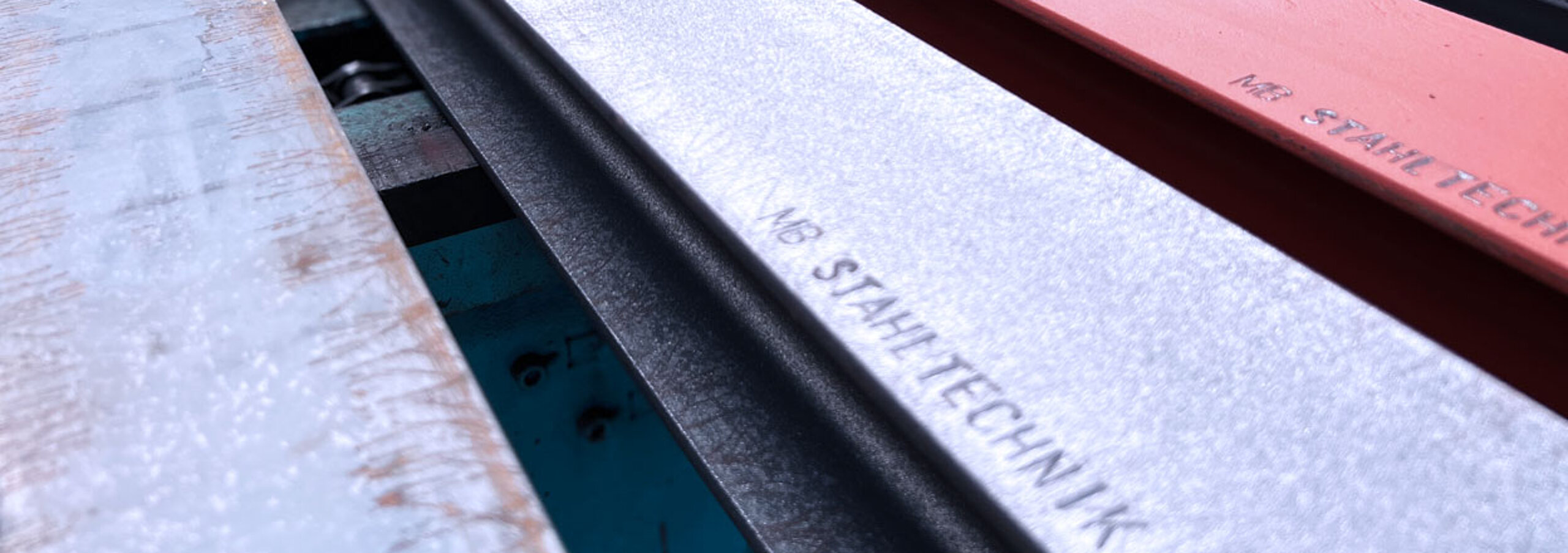 Drei verschiedenfarbige Stahlträger in die "MB Stahltechnik GmbH" eingraviert ist