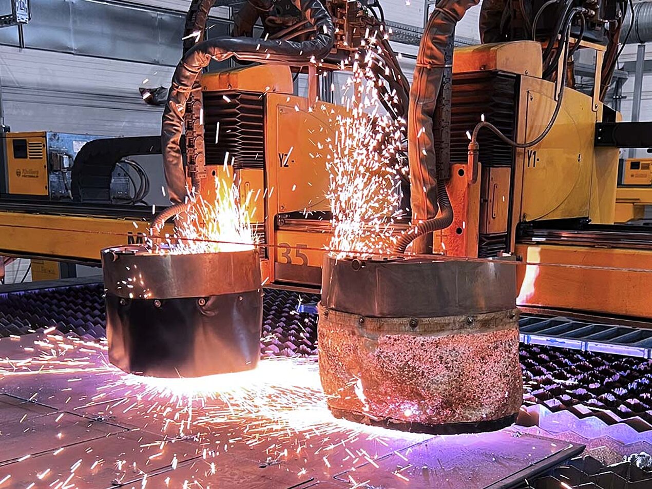 Zwei Roboteranlagen schneiden oder schweißen gleichzeitig an großen Metallzylindern, Funken fliegen.